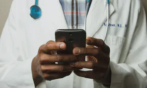 Doctor holding smartphone, only his hands and stethoscope hanging around his neck are in shot