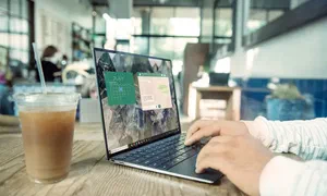 person using a laptop on a wooden table with a drink on the side