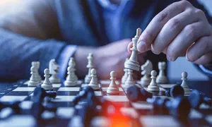 close up of chess pieces on a board with a hand lifting up the king