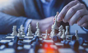 close up of chess pieces on a board with a hand lifting up the king