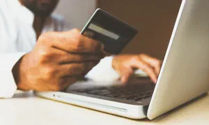 person entering their credit card details into a laptop, only their hands, the card and the laptop is visible