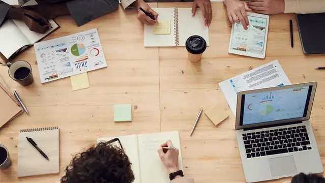 Top-down view of people collaborating across a table with laptops and notepads