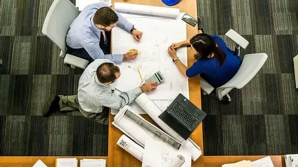 Top-down view of people collaborating across a table with large blueprint