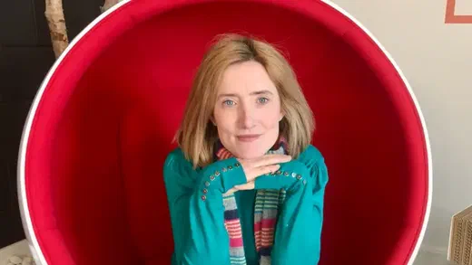 Ruth Kearney sitting in a red round chair with her hands clasped under her chin.