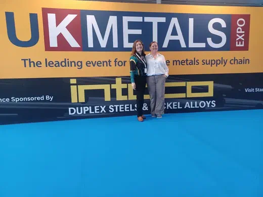 Two women standing in front of the UK Metals Expo banner, sponsored by Introco Duplex Steels & Nickel Alloys.