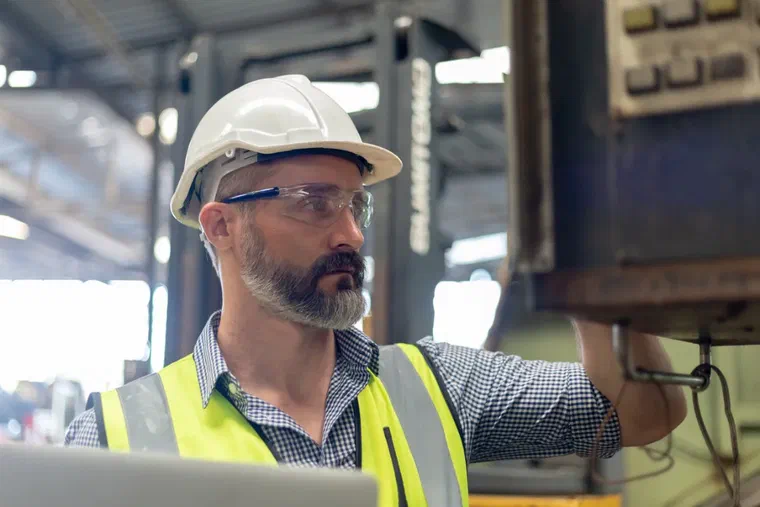 A quality manager in a hard hat and safety glasses inspecting equipment in a metals manufacturing facility