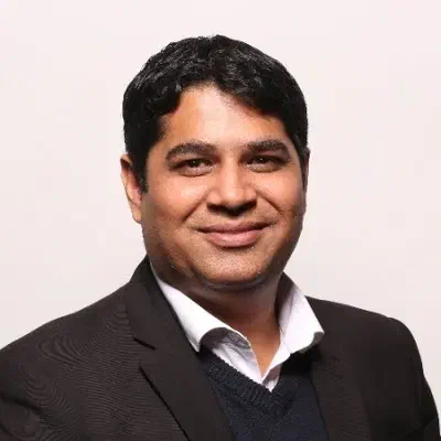 Gourav Tandon, smiling in a dark suit over a navy jumper