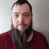 Mathew, a white man with short brown hair and a long brown beard, is looking toward the camera, in front of a white background