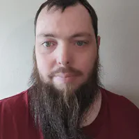 Mathew, a white man with short brown hair and a long brown beard, is looking toward the camera, in front of a white background
