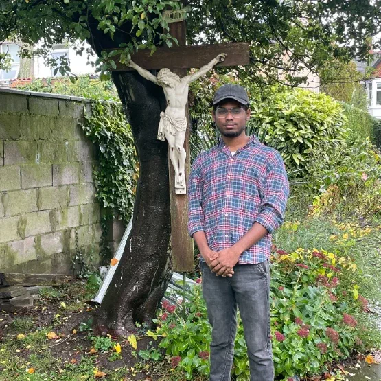 A photo of Remin standing in front of a crucifix in a garden