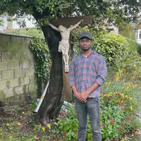A photo of Remin standing in front of a crucifix in a garden