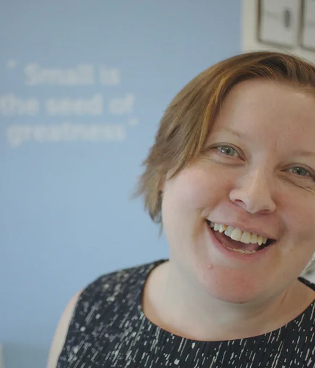 Steph Locke, a pale woman with short red hair, is standing slightly off-centre, smiling at the camera