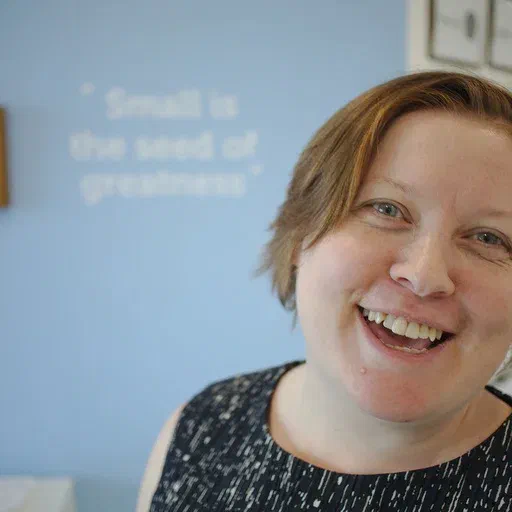 Steph Locke, a pale woman with short red hair, is standing slightly off-centre, smiling at the camera