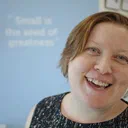 Steph Locke, a pale woman with short red hair, is standing slightly off-centre, smiling at the camera