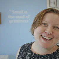 Steph Locke, a pale woman with short red hair, is standing slightly off-centre, smiling at the camera