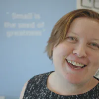 Steph Locke, a pale woman with short red hair, is standing slightly off-centre, smiling at the camera