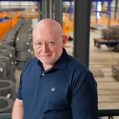 Tony Woods, a bald man with glasses in a navy polo shirt, smiling on a walkway above Midland Steel's fabrication floor